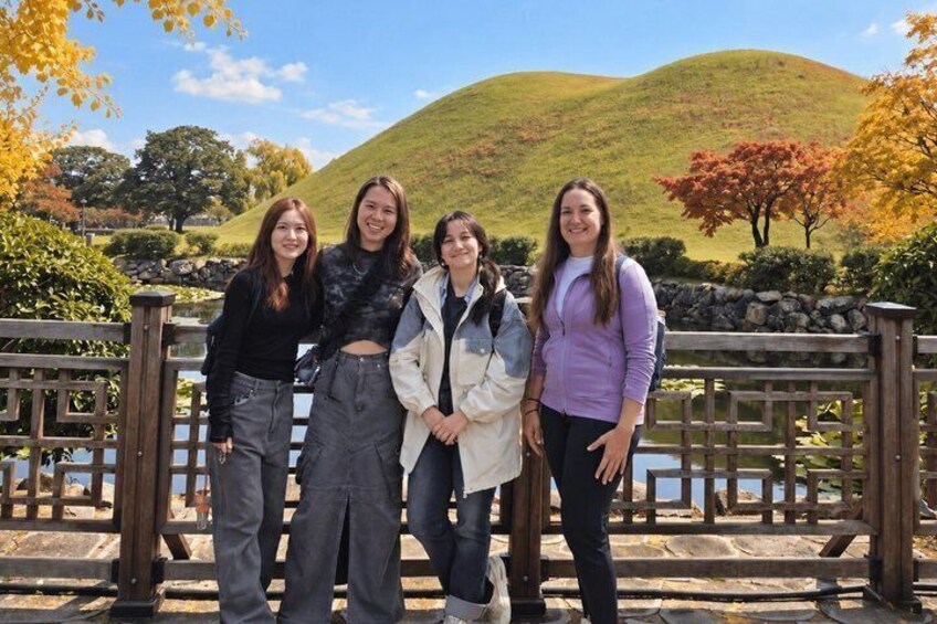 Four people standing in front of a wooden fence with a hilly landscape in the background. 3