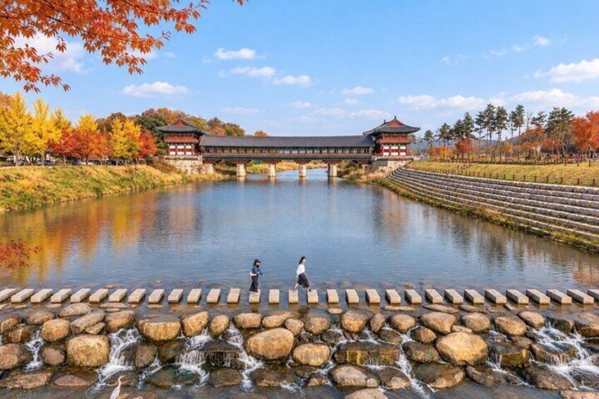 A traditional Korean bridge over a calm river, surrounded by autumn foliage and a stone walkway. 5