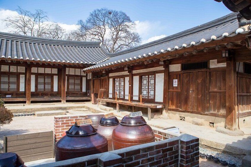 A traditional Korean building with wooden architecture, tiled roofs, and large ceramic jars. 5