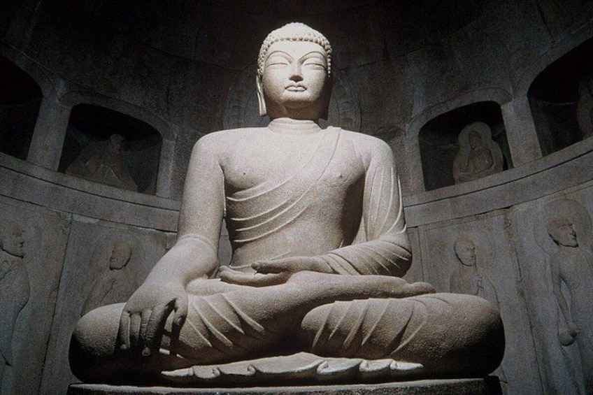 A large seated Buddha statue in a temple with stone carvings on the walls. 2