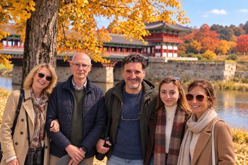 A group of people standing in front of a traditional building with a river and autumn foliage in the background. 1