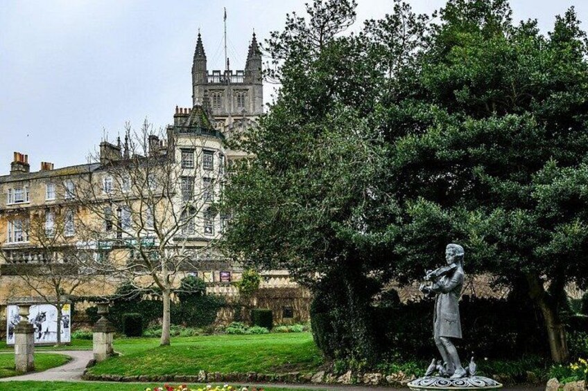 A statue of a person playing a flute, a large tree, and a historic building in the background. 4