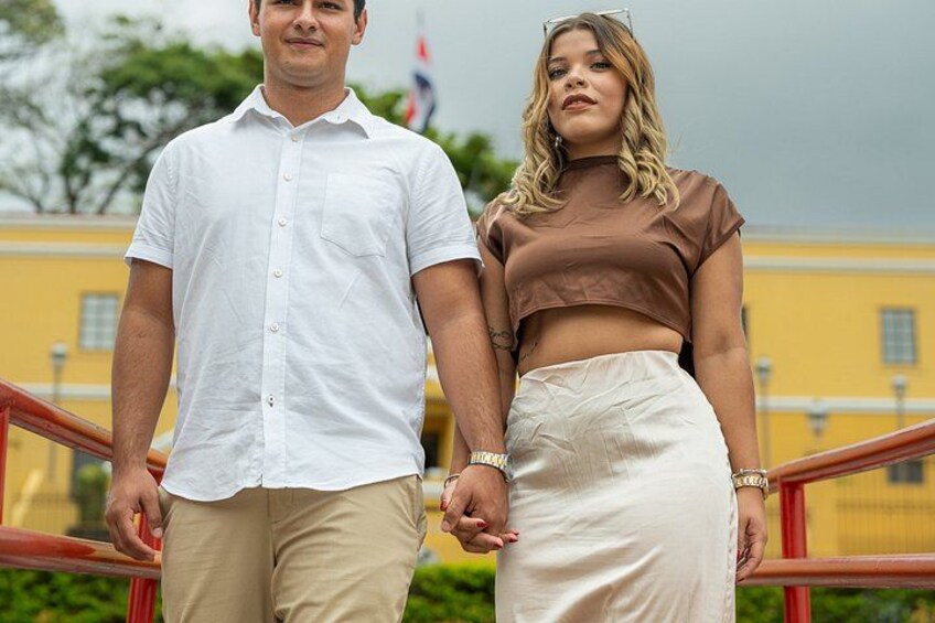 A man and a woman holding hands on a staircase with a yellow building in the background. 1