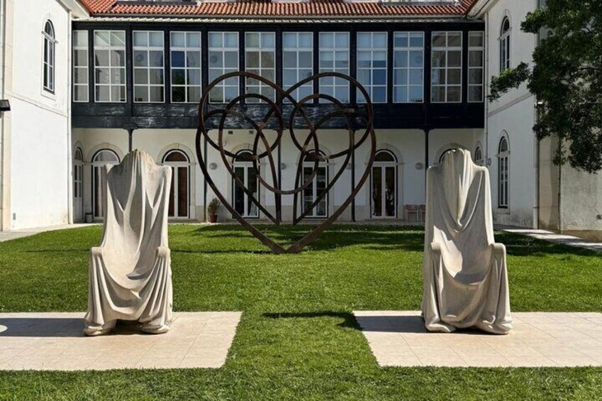 A building with a heart-shaped sculpture in the center, two draped statues on either side, and a well-maintained lawn. 3