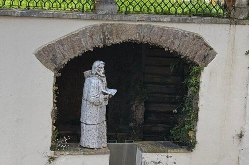 A stone statue of a robed figure reading a book, set in a niche with a stone arch above it. 2