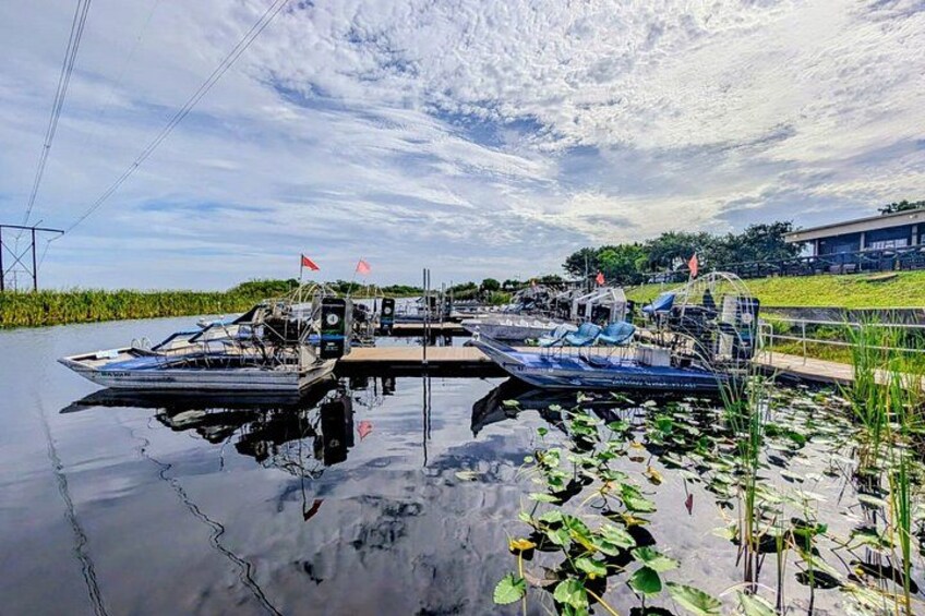 A calm waterway with boats docked at a pier, surrounded by greenery and a clear sky. 1