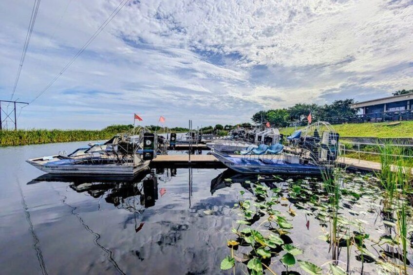 A calm river with boats docked at a pier, surrounded by greenery and a clear sky. 1