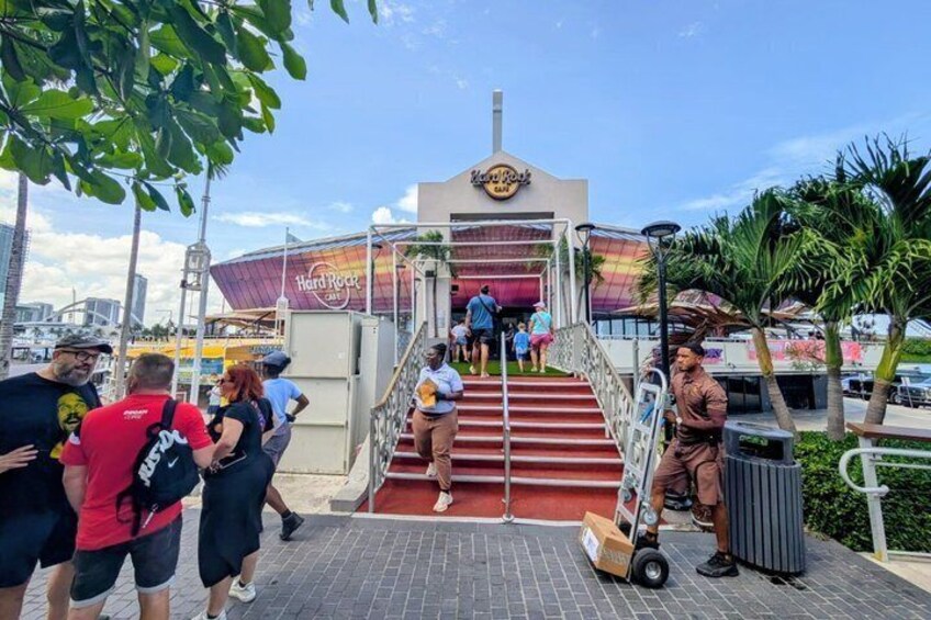 A Hard Rock Cafe entrance with people ascending stairs, palm trees, and a clear sky. 1