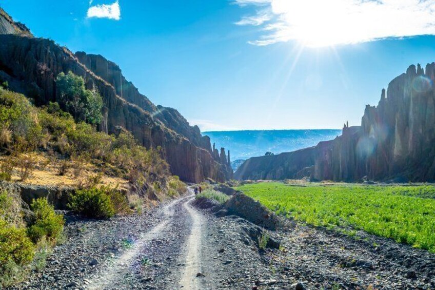 A rugged landscape with a dirt road leading towards a coastal area, surrounded by cliffs and sparse vegetation. 3
