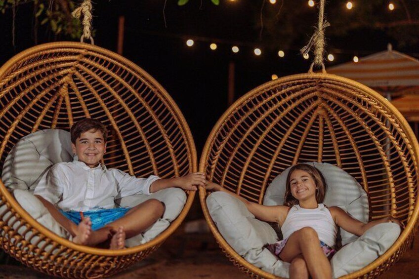 Two children in wicker chairs with cushions, outdoors at night. 2