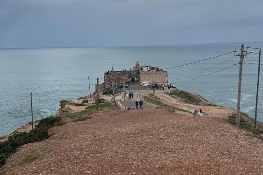 A coastal fortification with a lighthouse, a dirt path, and a few people walking. 3