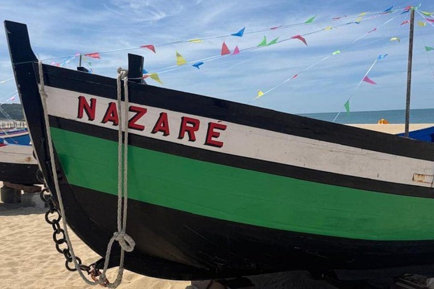 A boat named NAZARE on a sandy beach with colorful flags in the background. 1
