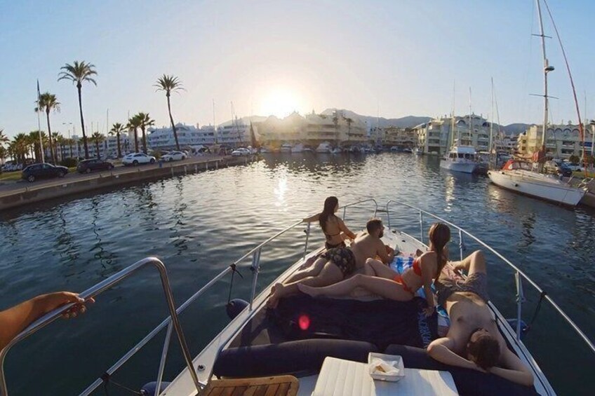A boat with people relaxing on the deck, a marina with boats, and palm trees in the background. 3