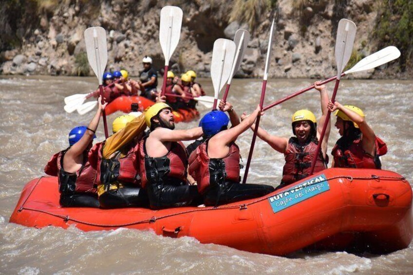 A group of people in a red inflatable raft on a river, wearing helmets and life jackets. 5