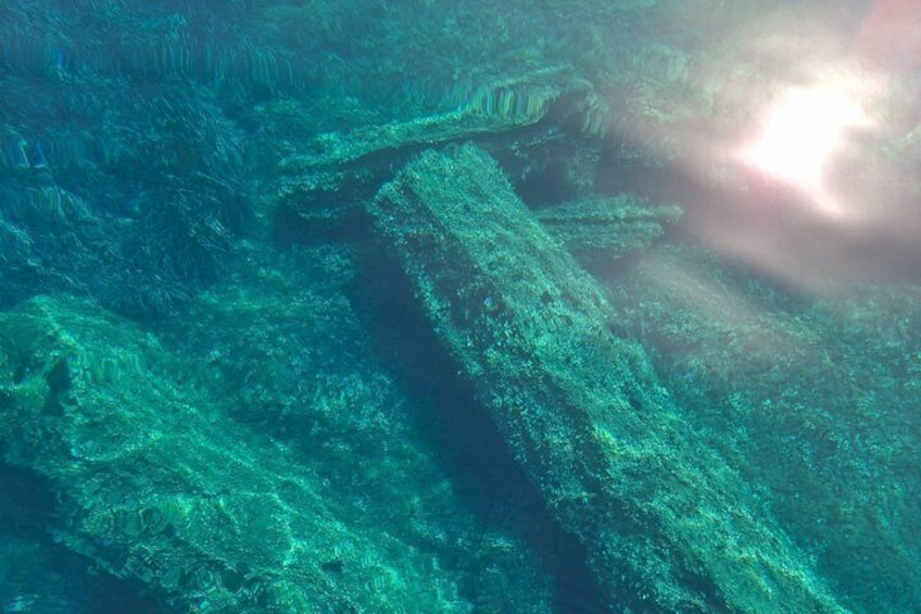 An underwater scene with a large, sunlit wreck and marine growth. 5