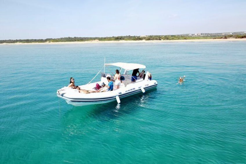 A boat on turquoise water with people on board and a beach in the background. 1