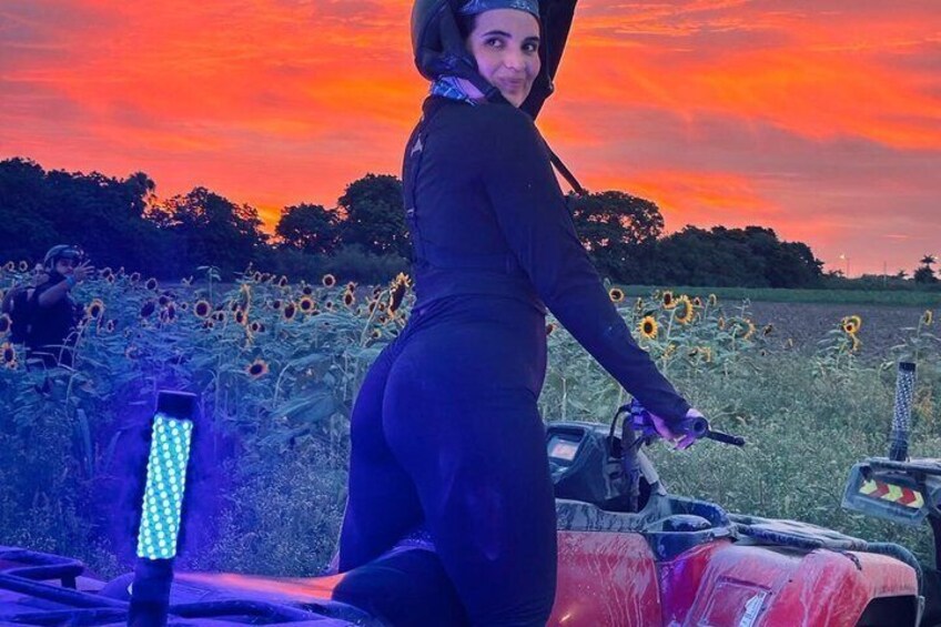 A person riding a red ATV in a field of sunflowers during sunset. 1