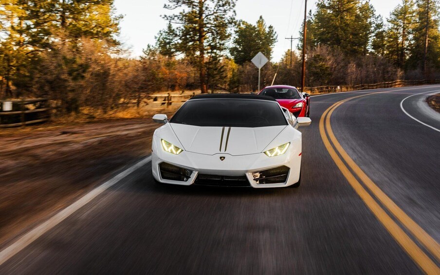 A white sports car driving on a curvy road surrounded by trees. 1