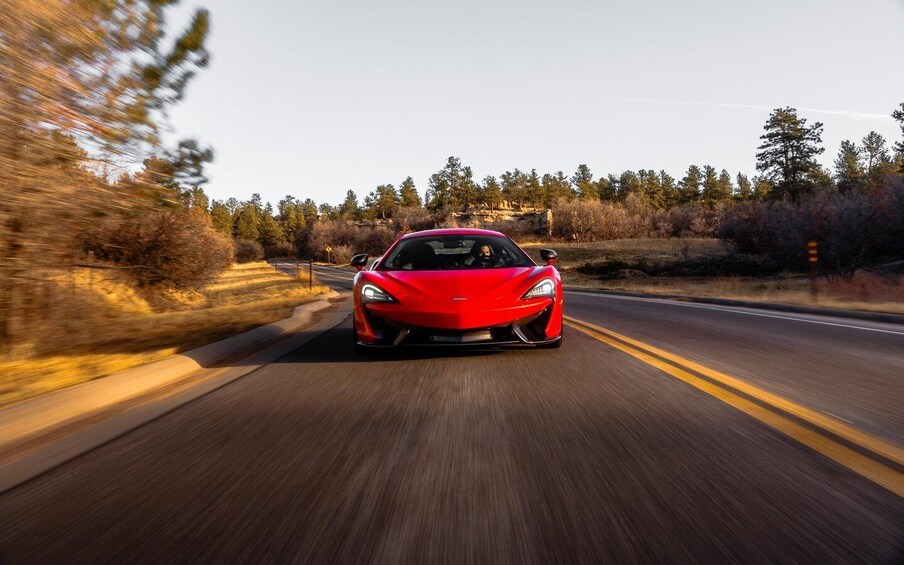 A red sports car driving on a road with a forested landscape in the background. 4