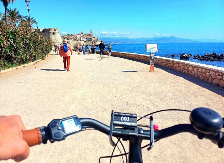A paved walkway with people walking, a clear blue sky, and a distant view of a coastal town. 5