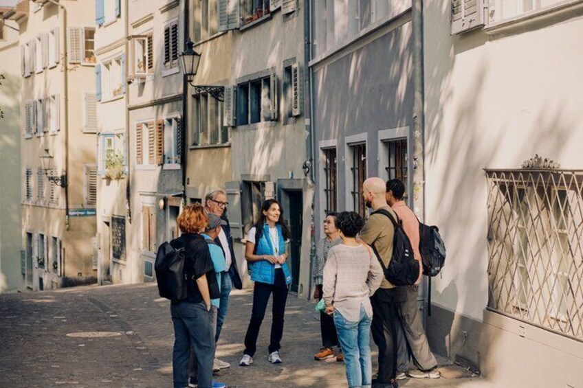 A group of people standing on a street in a European city, with buildings and a gate in the background. 2