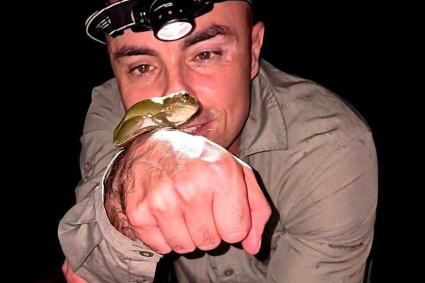 A person wearing a light-colored shirt with a dark tie, holding a small object close to their face. 1