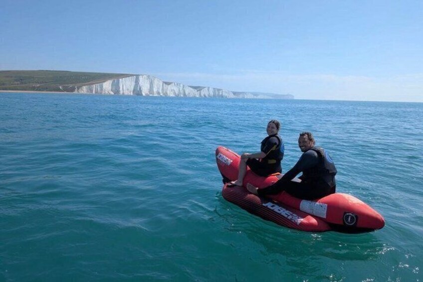 Two people on a red jet ski in the ocean with white cliffs in the background. 2