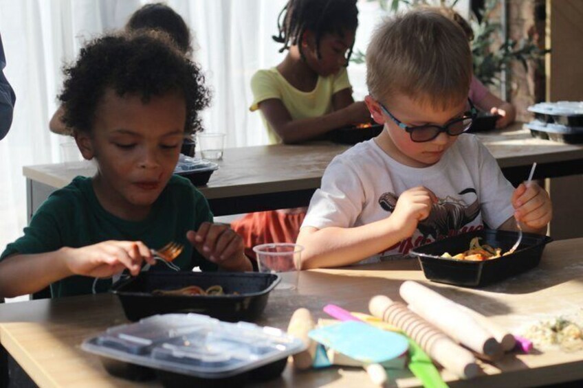 Children eating at a table with food containers and utensils. 4