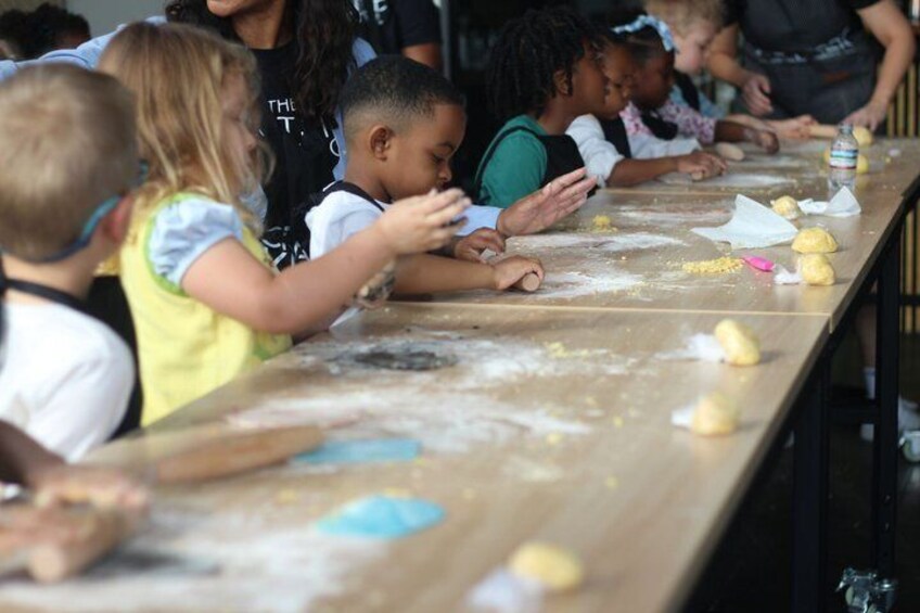 Children engaged in a dough rolling activity at a long table. 3