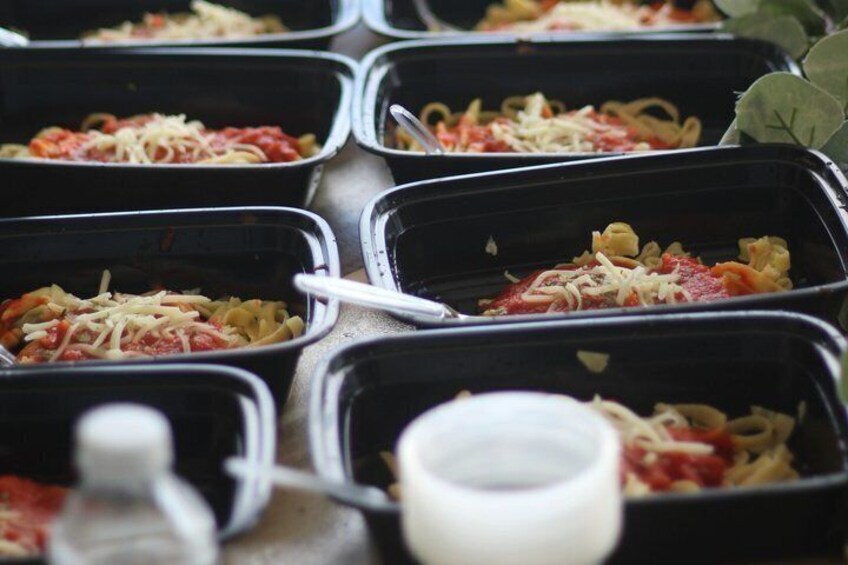 Multiple black food containers with pasta dishes topped with cheese and tomato sauce. 2
