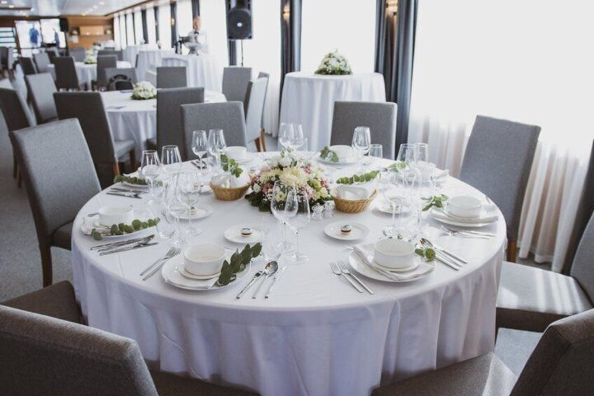 A round dining table set with white tablecloths, plates, glasses, and a centerpiece of flowers. 2
