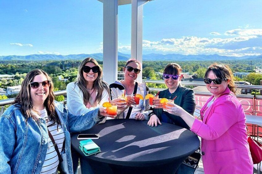 Un grupo de personas brindando con bebidas en una mesa, con una vista panorámica al fondo. 3