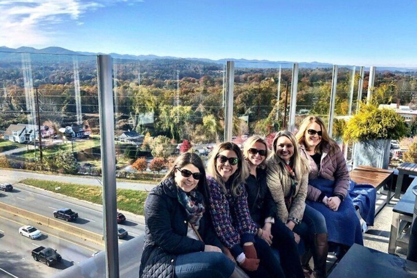 A group of people sitting on a balcony overlooking a road and autumn foliage. 5