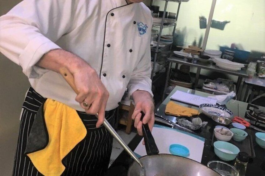 A chef in a kitchen with a pot on the stove, a cutting board, and various kitchen utensils. 2