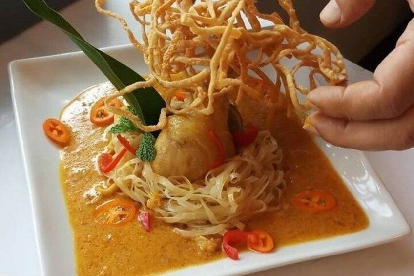 A plate of noodles with a piece of meat, garnished with sliced red chili and green herbs. 5