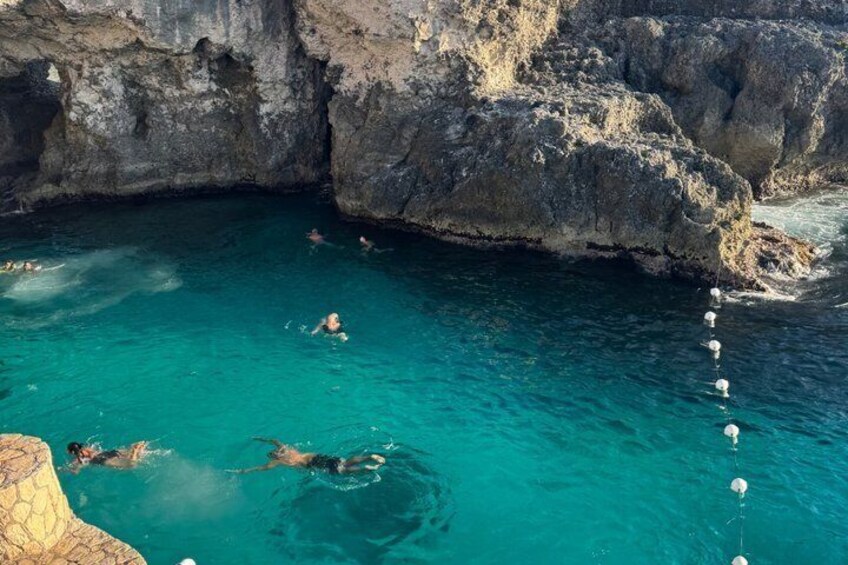 A clear blue sea with swimmers and a rocky cliff. 3