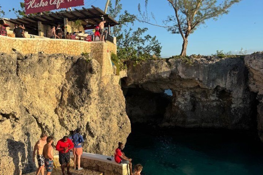 A rocky cliff with a café named 'Riche Café' and a clear blue pool at the base. 4