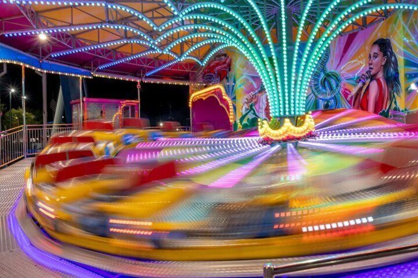 A brightly lit amusement ride with a colorful, illuminated canopy and a central spinning platform. 3
