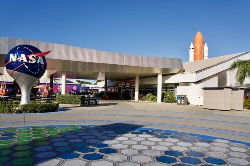 A NASA building with a hexagonal floor pattern, a large NASA logo, and a rocket structure in the background. 1