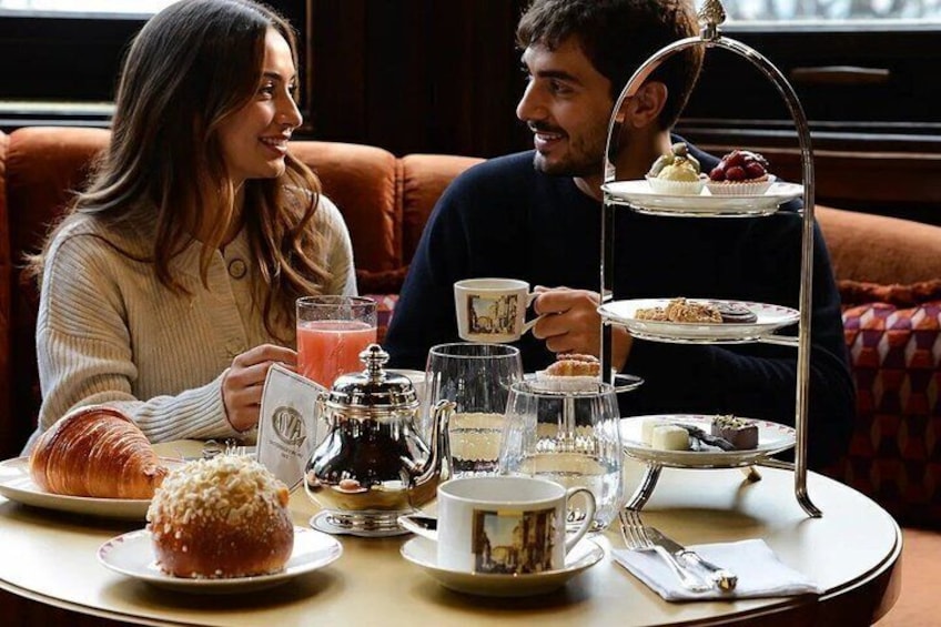 A couple sitting at a table with a tiered tea service, pastries, and a croissant. 1