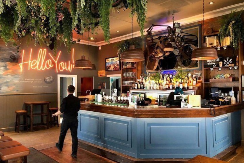 A bar with a blue counter, hanging plants, and a neon sign that reads 'Hello You!' 5
