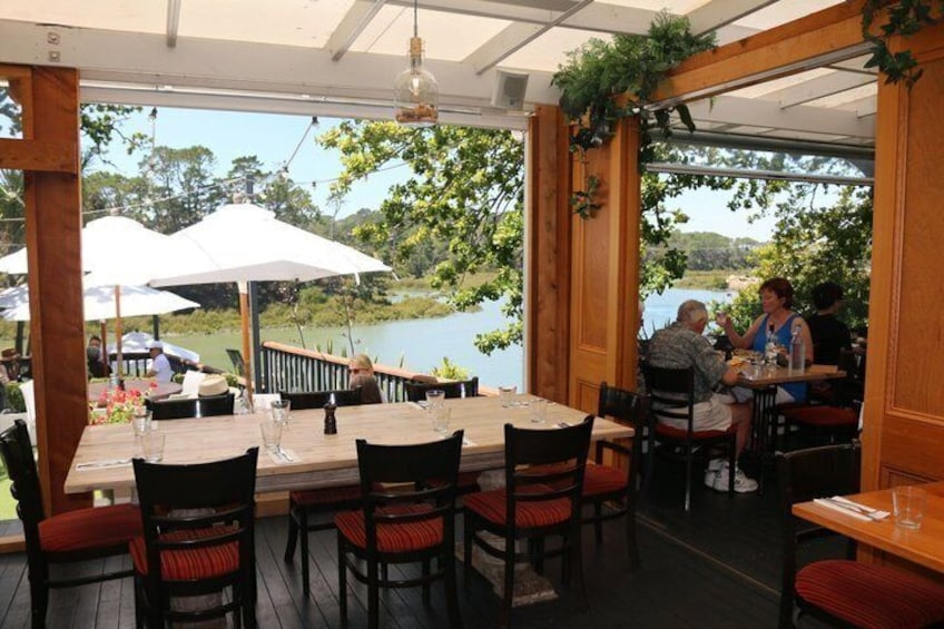 An outdoor restaurant with wooden tables and chairs, white umbrellas, and a view of a lake. 3