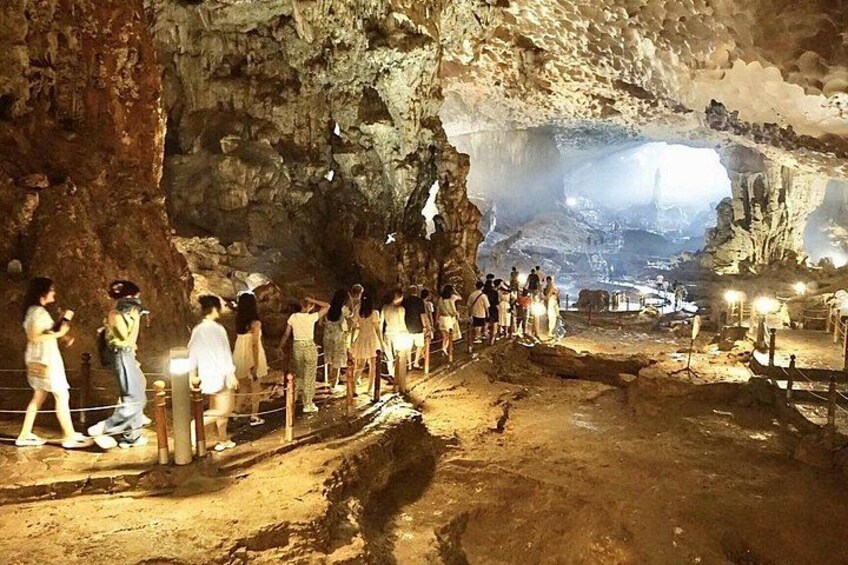 A cave with tourists walking on a path, a large rock formation, and a light source at the end of the cave. 3