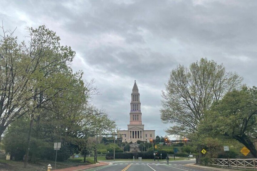 A historic building with a tall tower, surrounded by trees and a street. 2