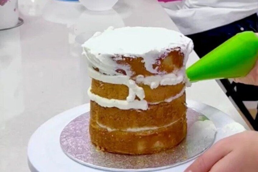 A layered cake with white frosting being piped on top. 4