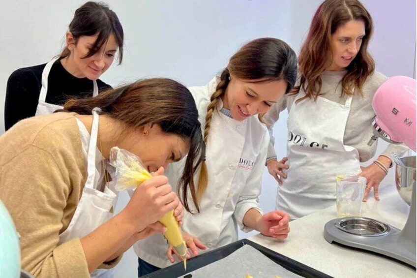 Four people in a kitchen, one squeezing a yellow substance into a mold. 1