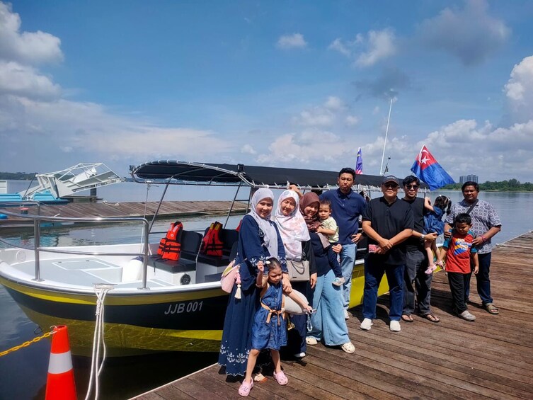 A group of people on a dock by a boat with a flag, a clear sky, and calm water. 4