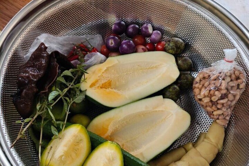 A colander with various fresh produce including halved melons, cherry tomatoes, green olives, and herbs. 3