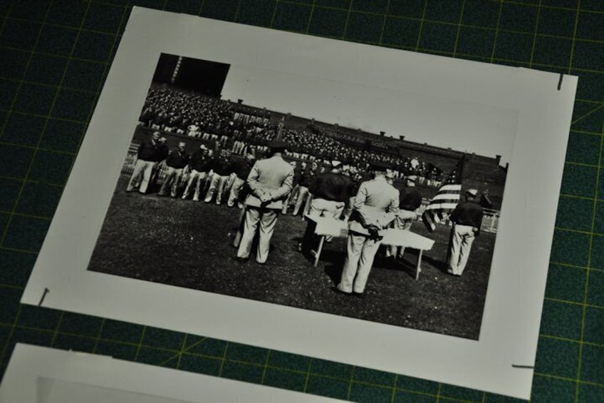 A black and white photograph of a group of people seated on chairs in a stadium. 5