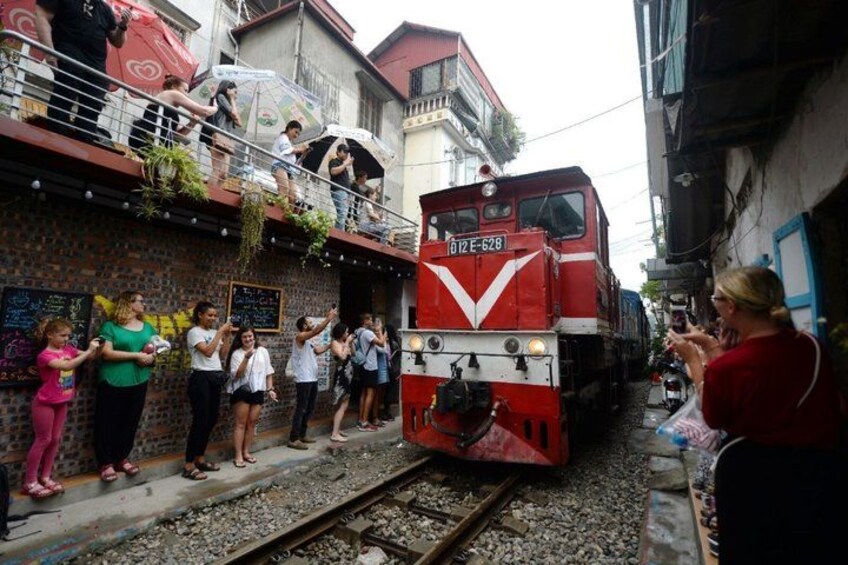 A red train on tracks, people standing on a platform, and a building with graffiti. 3